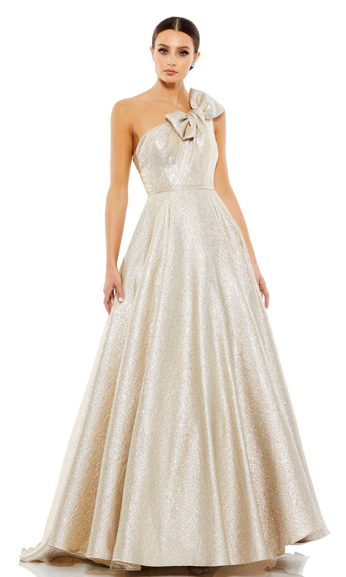 A woman wears the Long Formal Dress 67890 by Mac Duggal, a shimmering, floor-length one-shoulder gown with a statement bow at the neckline, styled as an elegant metallic ball gown.